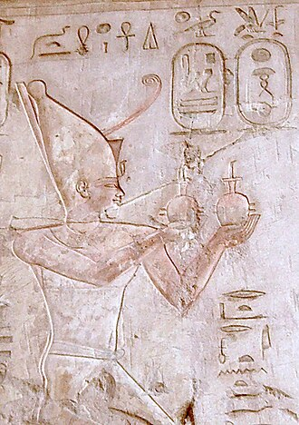 Relief représentant le pharaon Psammétique Ier faisant une offrande aux dieux – Tombe de Pabasa à Thèbes. 
Description plus longue : gravé sur une pierre ocre, un pharaon égyptien se tient torse nu et en pagne. Il porte une longue couronne en forme à peu près de cône. Il lève des objets sphériques dans ses mains, probablement des offrandes. Des cartouches indiquent son nom en hiéroglyphes.
