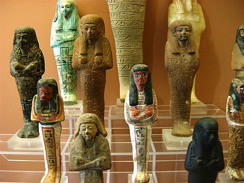 Ouchebtis égyptiens : de petites statuettes d'argile ou de pierre à l'effigie d'un défunt dans son sarcophage, ciselées et colorées (ici, de blanc, brun, ocre, avec des touches de bleu, de jaune et de rouge ; certains ouchebtis sont de pierre noire ou bleu clair)